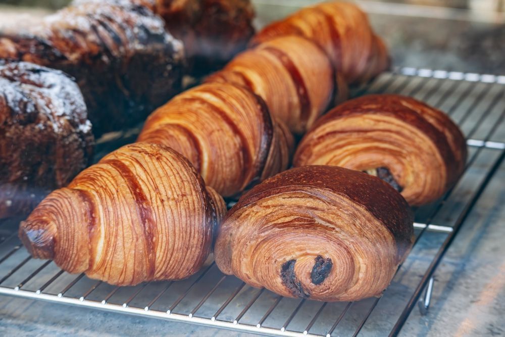Pastries on a metal rack; including croissants and chocolate croissants, various shades of brown.
