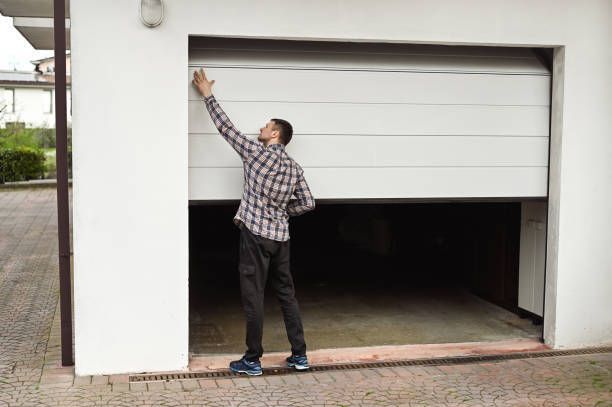 A man is opening a garage door with his hand.