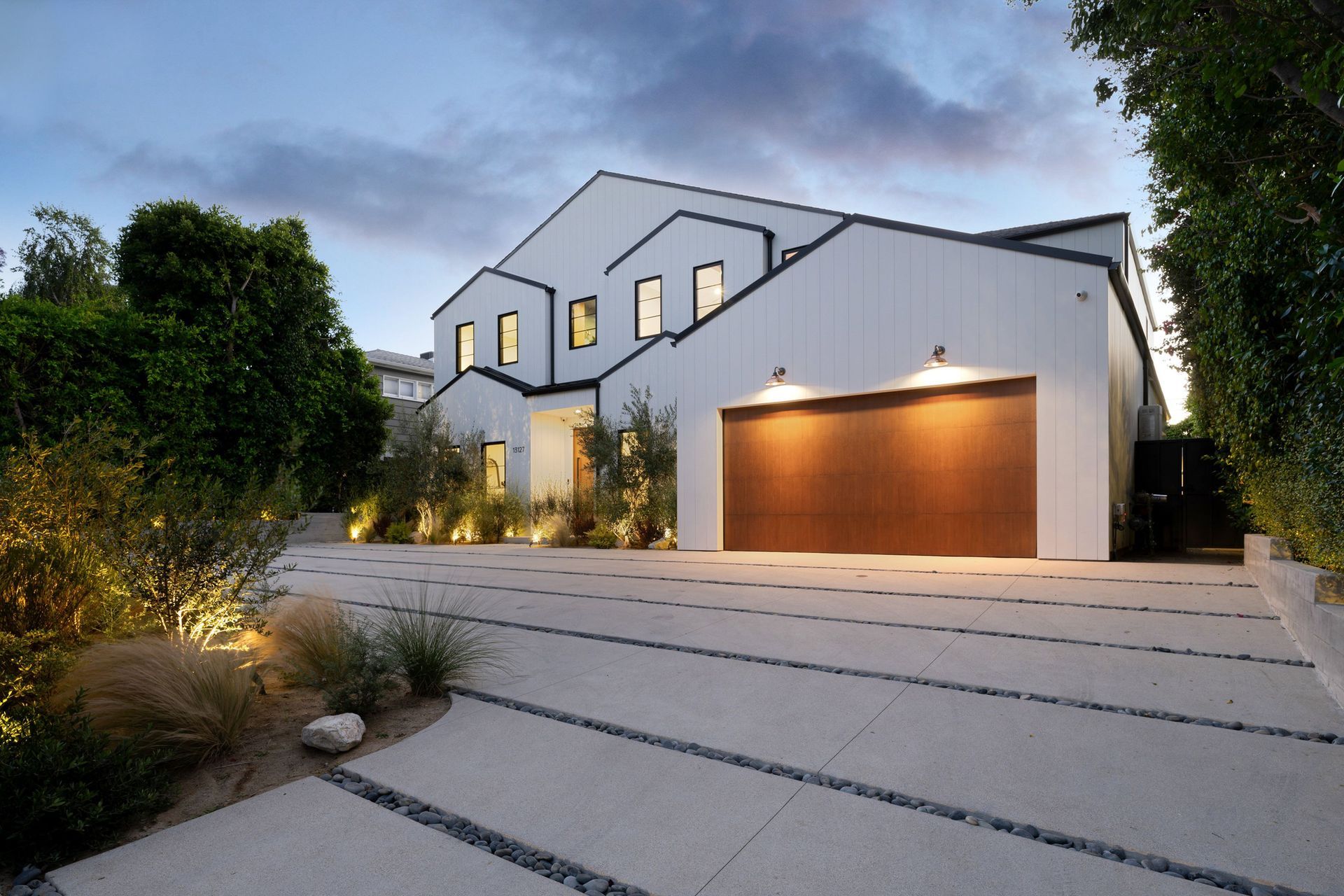 A modern house exterior with a wooden garage door and landscaped driveway at dusk