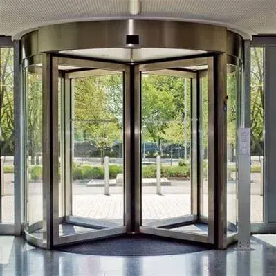 A revolving glass door in a building with trees in the background.