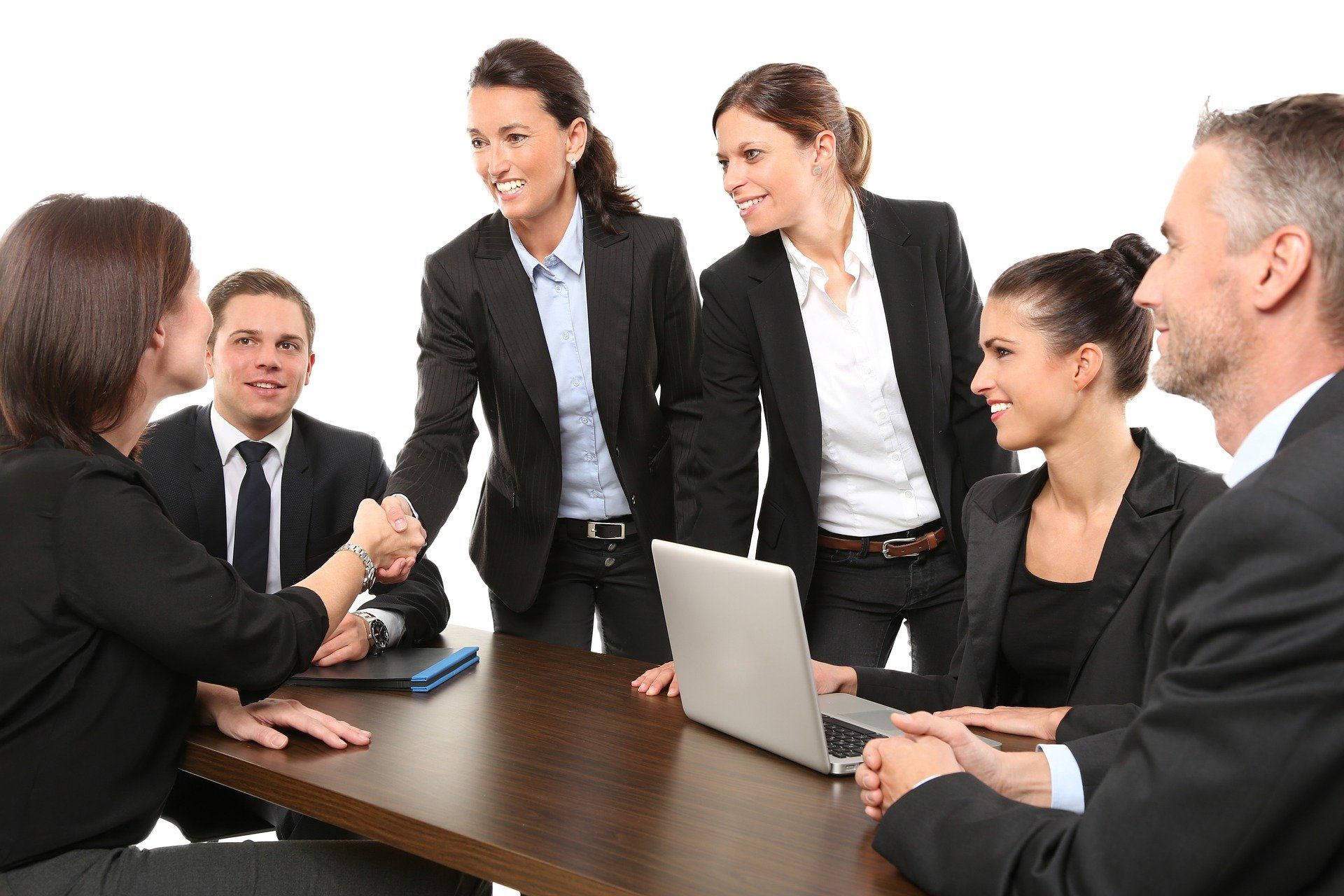 A group of business people are shaking hands at a table with a laptop.