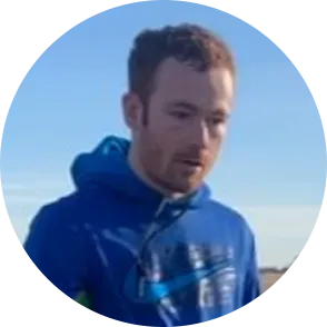 Man in blue hoodie looking down, outdoors.