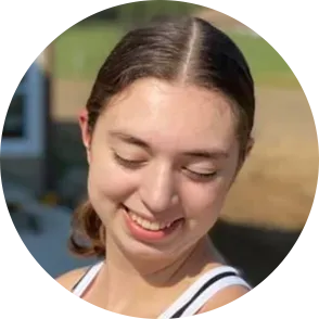 Young woman with brown hair, smiling with closed eyes, outdoors.