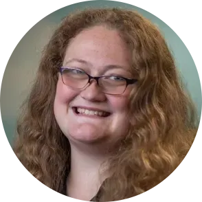 Woman with curly brown hair and glasses smiles.