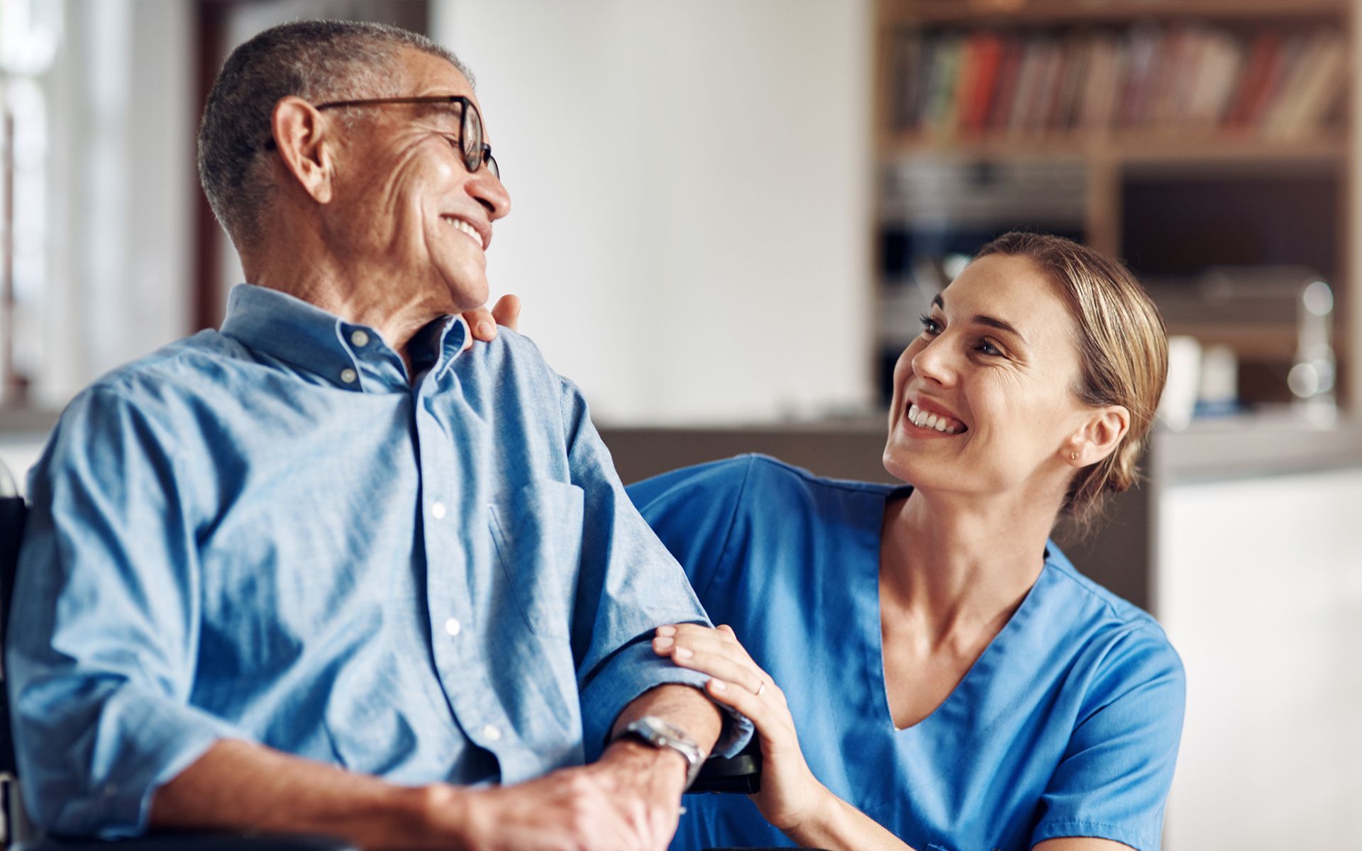A nurse is holding the hand of an elderly man in a wheelchair.