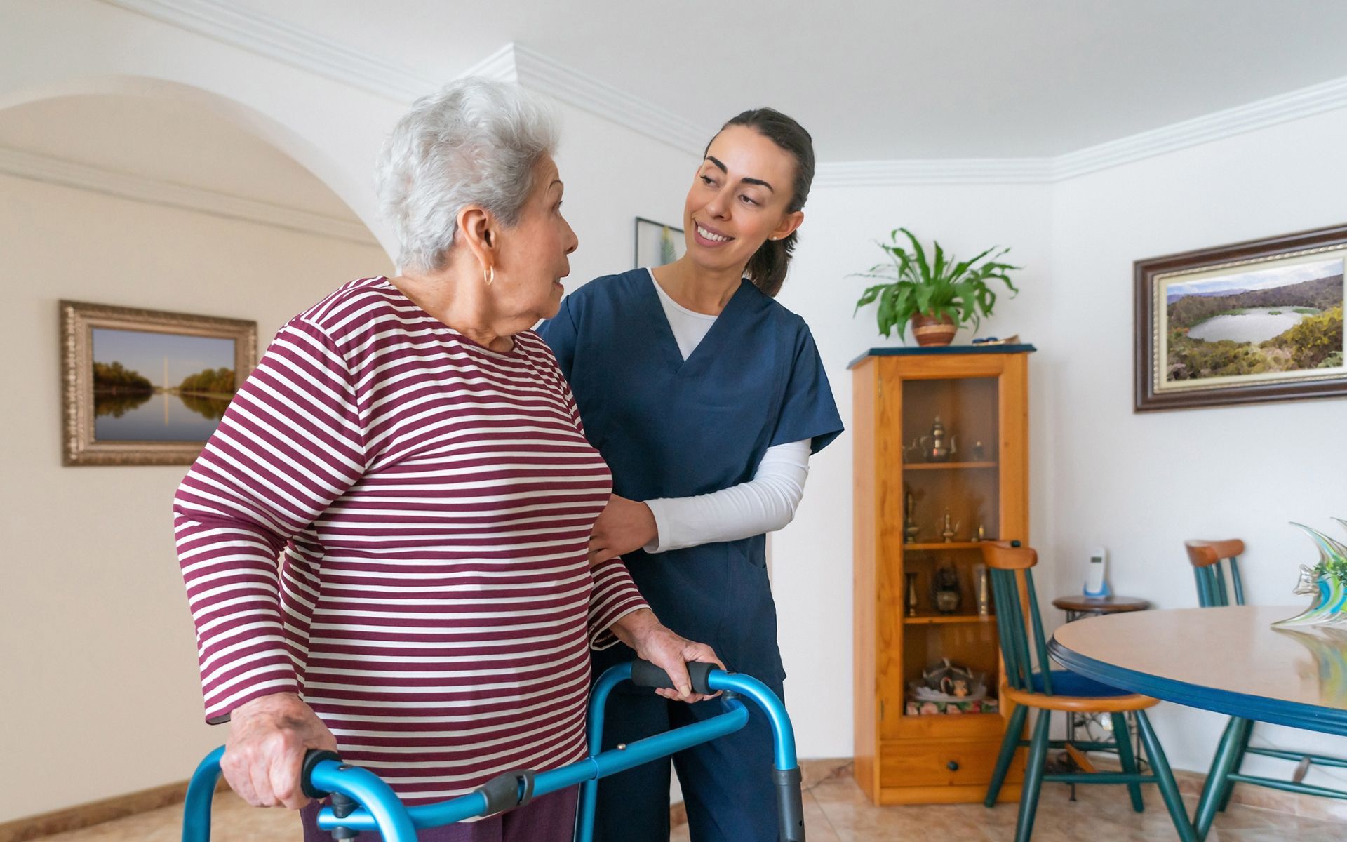 A nurse is helping an elderly woman with a walker in a living room.