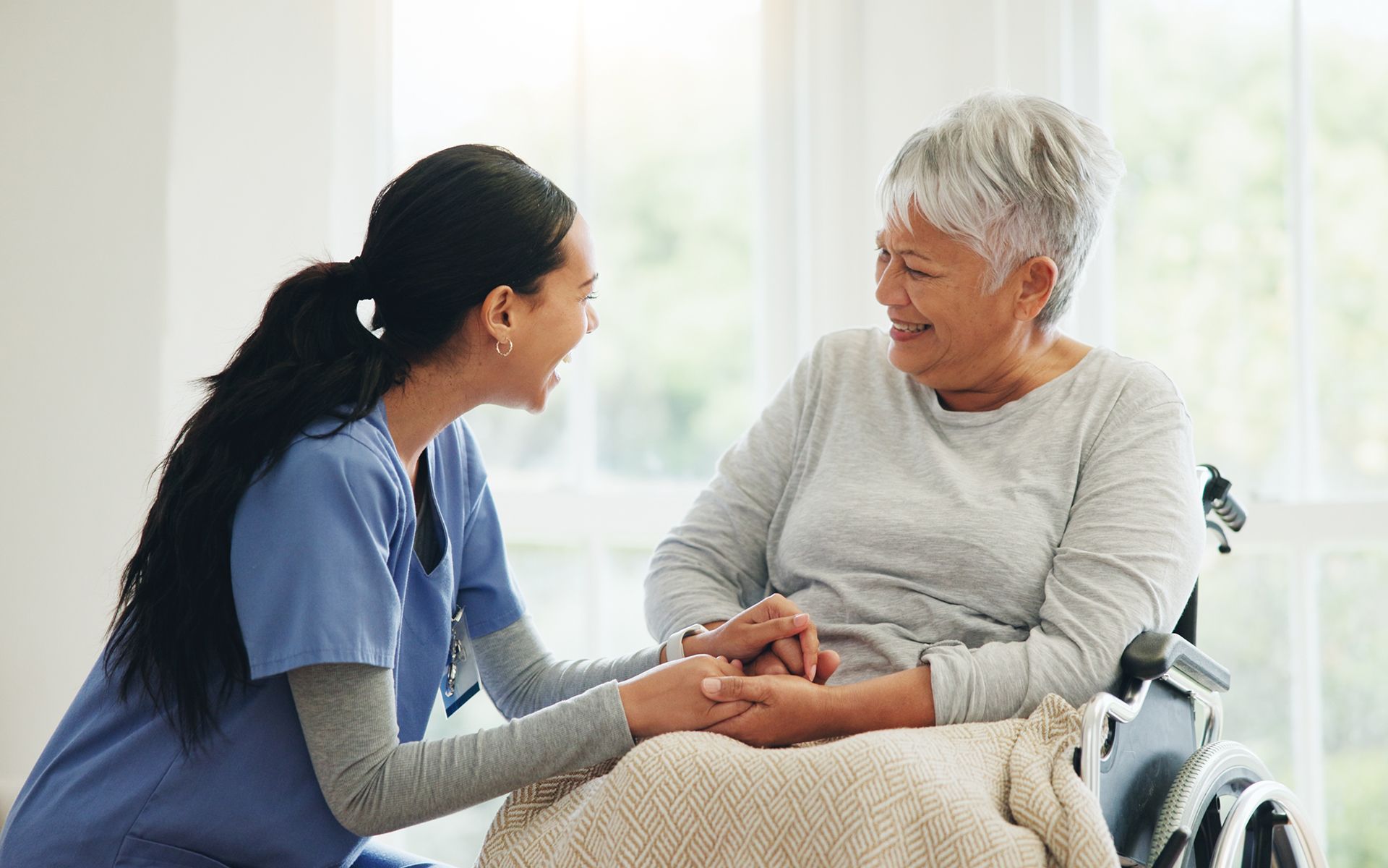 A nurse is holding the hand of an elderly woman in a wheelchair.