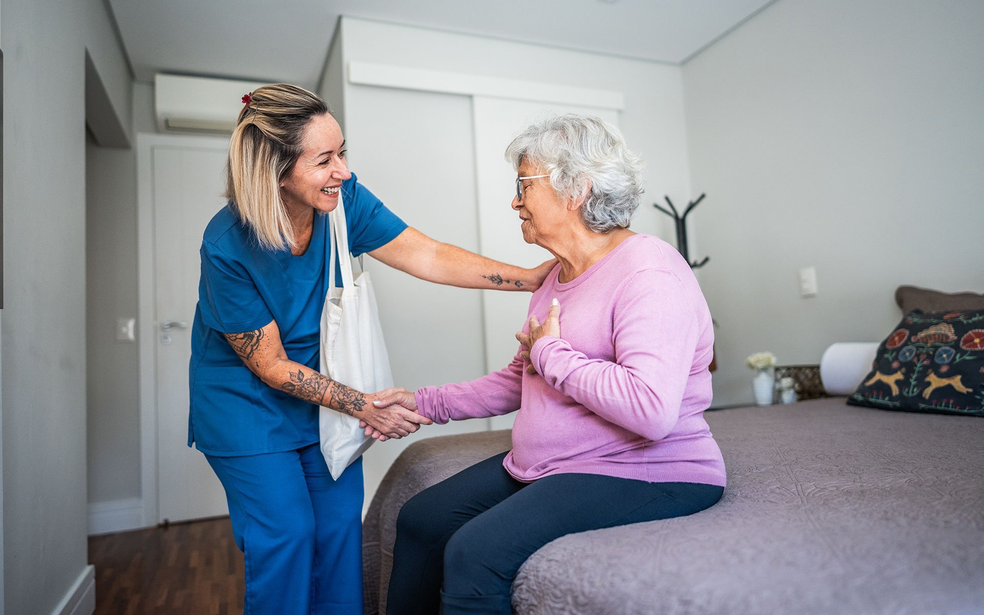 A nurse is helping an elderly woman sit on a bed.