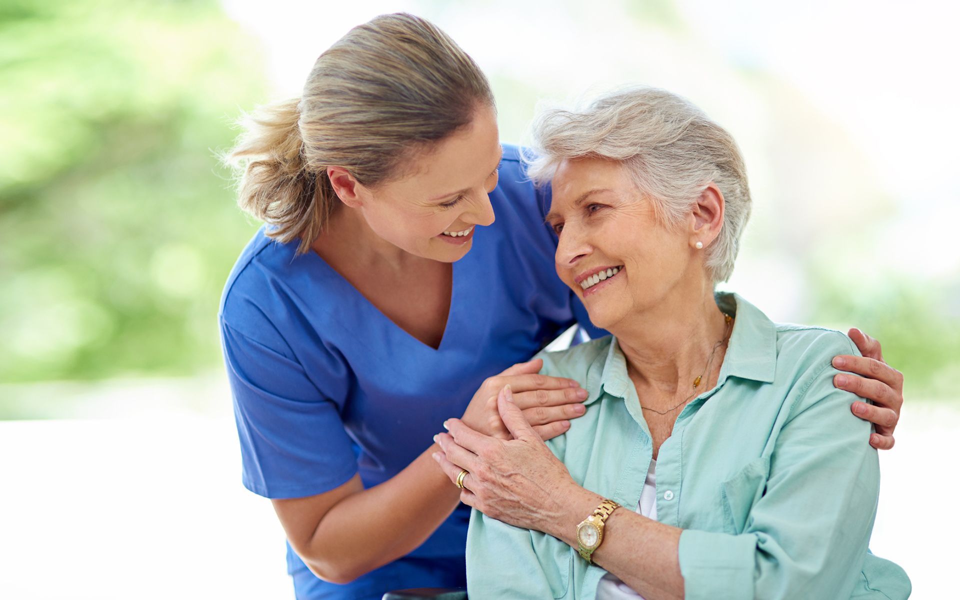 A nurse is hugging an elderly woman in a wheelchair.