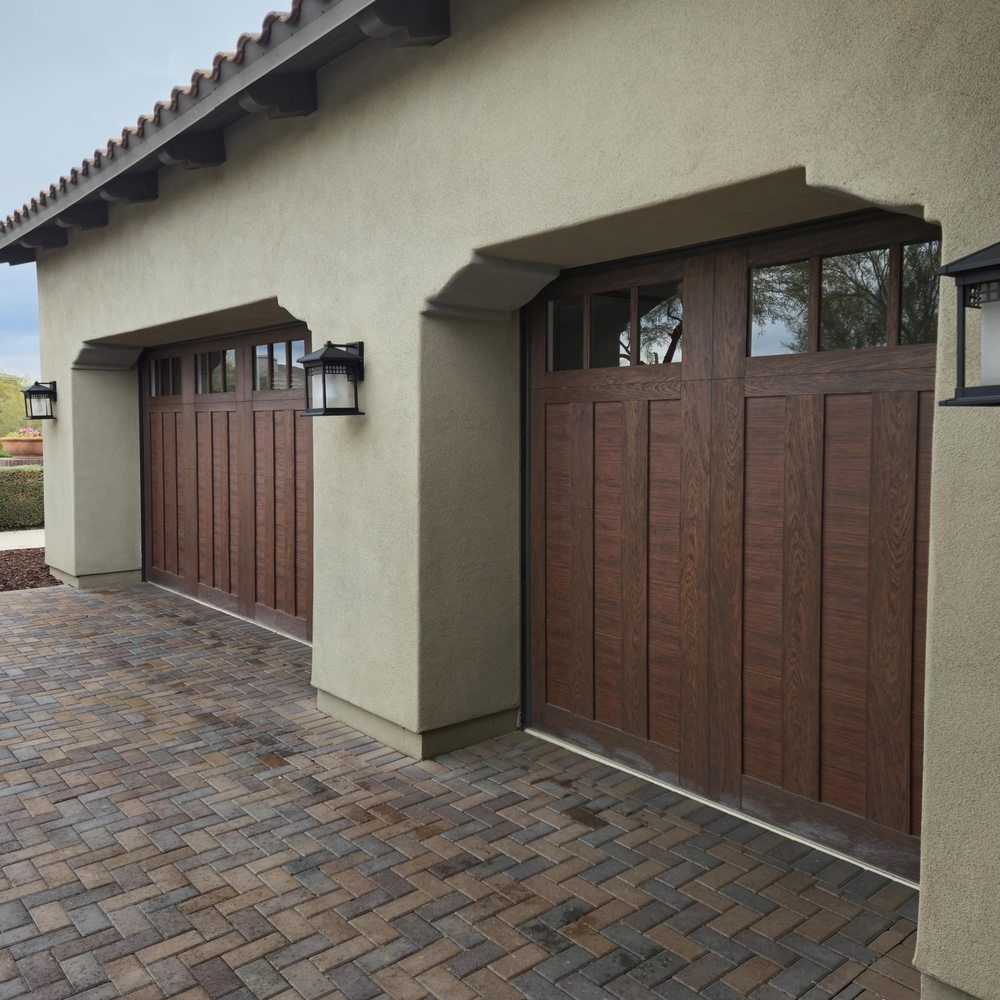 Two wooden garage doors on a brick driveway