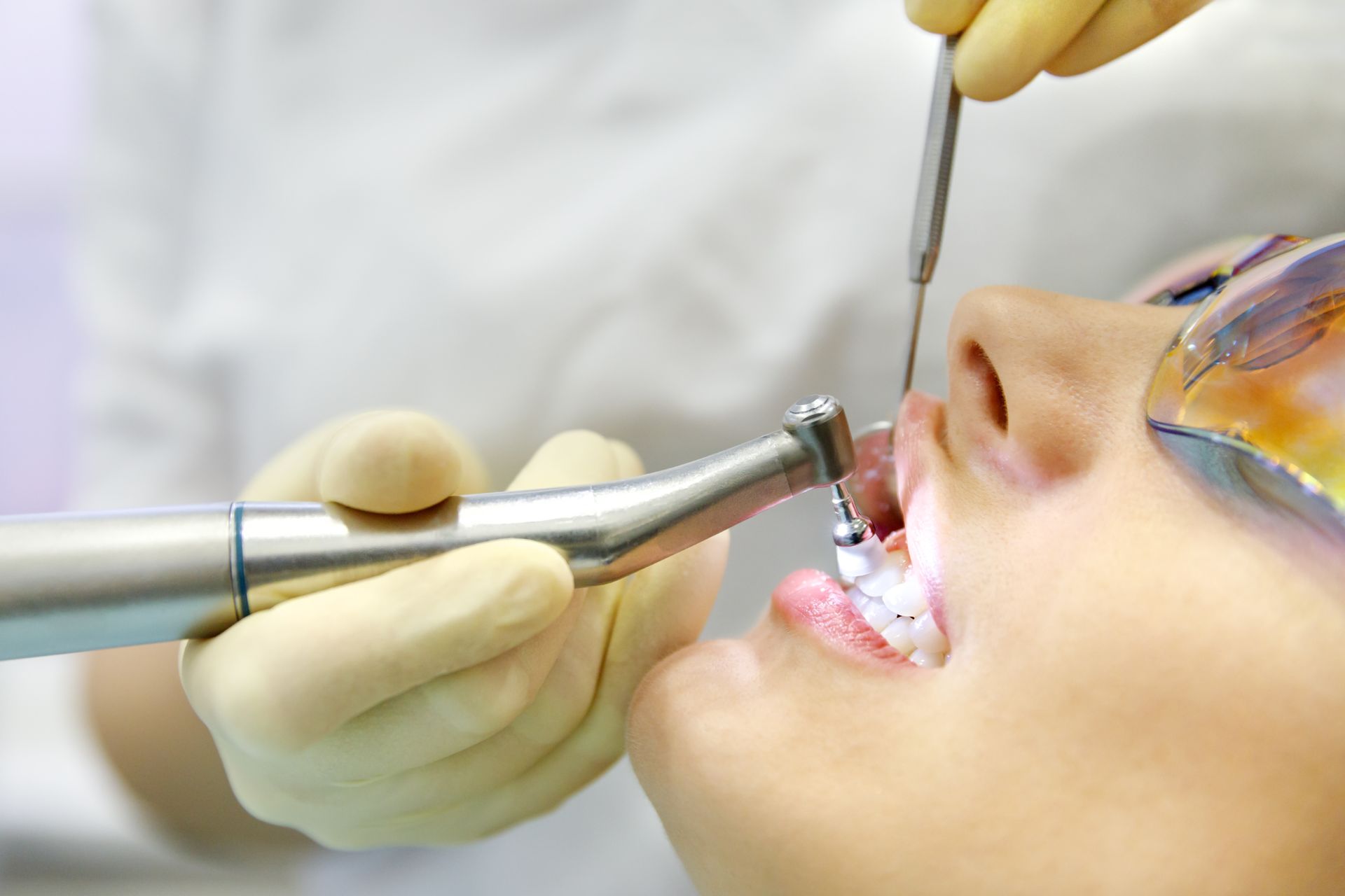 Dentist performing dental work on a patient's open mouth with tools.