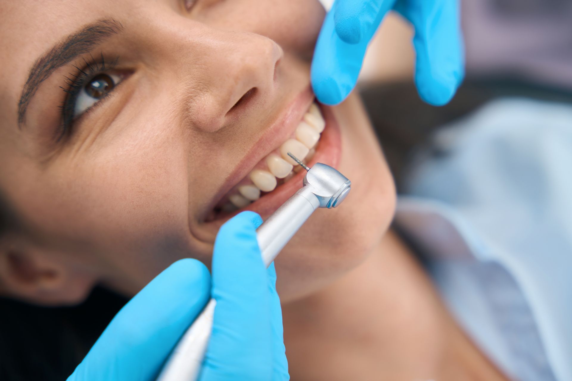 Dentist working on a patient's teeth. Patient smiles while being examined with a dental tool. Gloves are blue.