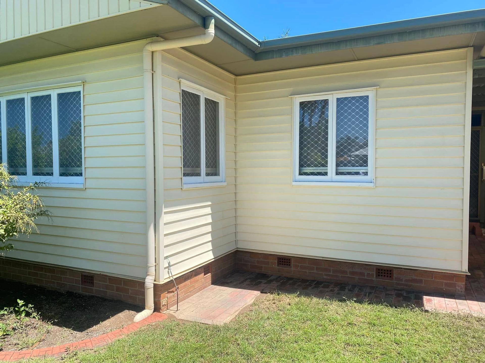 The corner of a light yellow house with white-framed windows, white guttering, and a brick foundation. — CPR Exterior Cleaning in Bundaberg South, QLD