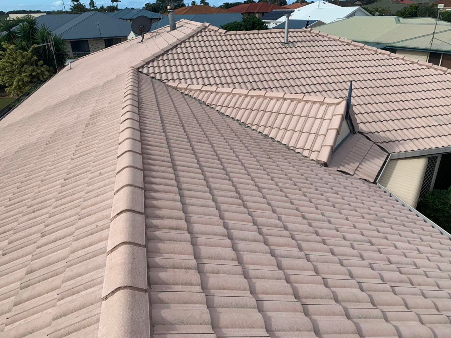 A high-angle view of a residential roof with light tan concrete tiles and dark ridge capping on a sunny day. — CPR Exterior Cleaning in Bundaberg West, QLD