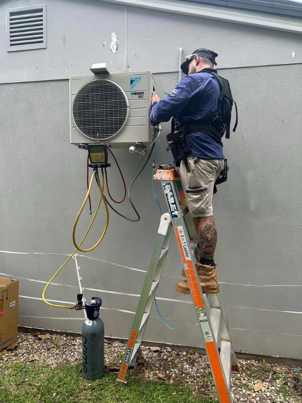 A Man is Standing on a Ladder Fixing an Air Conditioner — Eclipse Air Conditioning and Refrigeration in Trinity Beach, QLD