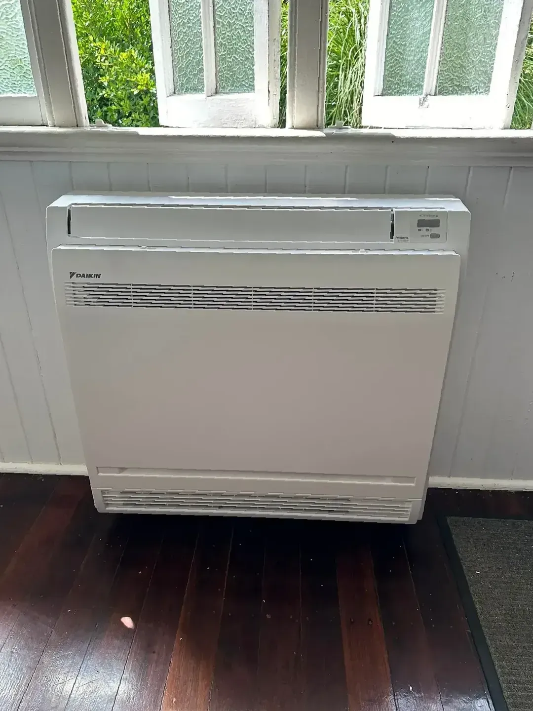 A White Air Conditioner is Sitting on a Wooden Floor — Eclipse Air Conditioning and Refrigeration in Trinity Beach, QLD
