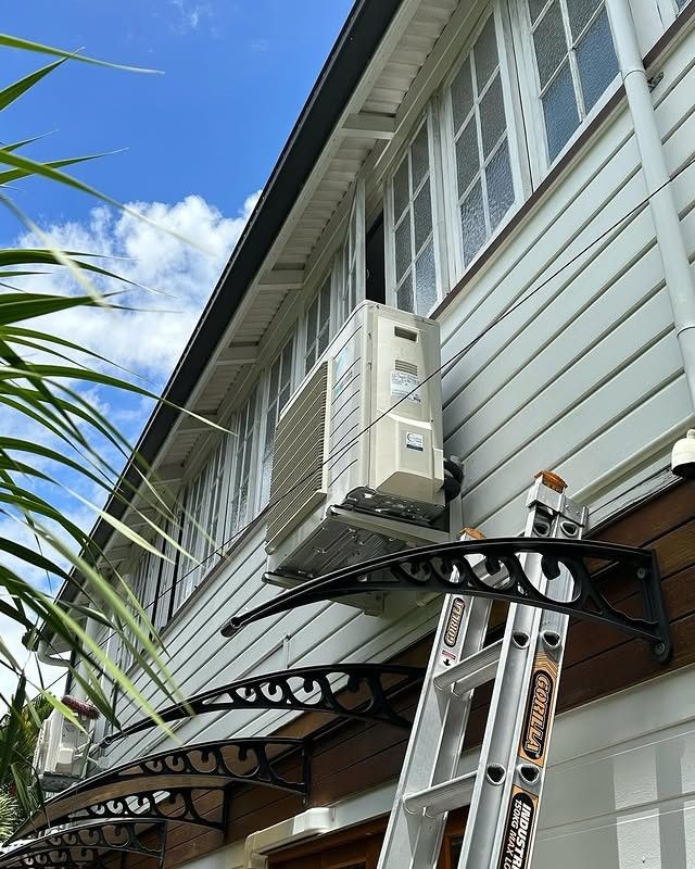 A Person is Standing on a Ladder Next to a Large Air Conditioner — Eclipse Air Conditioning and Refrigeration In Redlynch, QLD