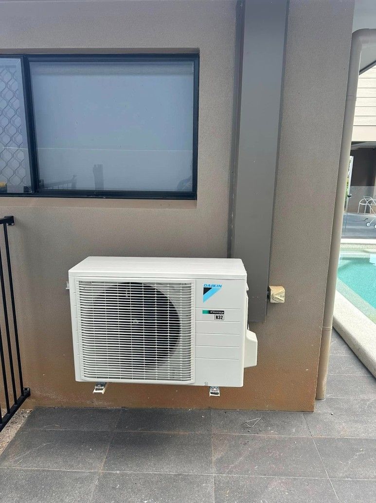 A White Air Conditioner is Mounted on the Side of a Building Next to a Wind — Eclipse Air Conditioning and Refrigeration In Smithfield, NSW