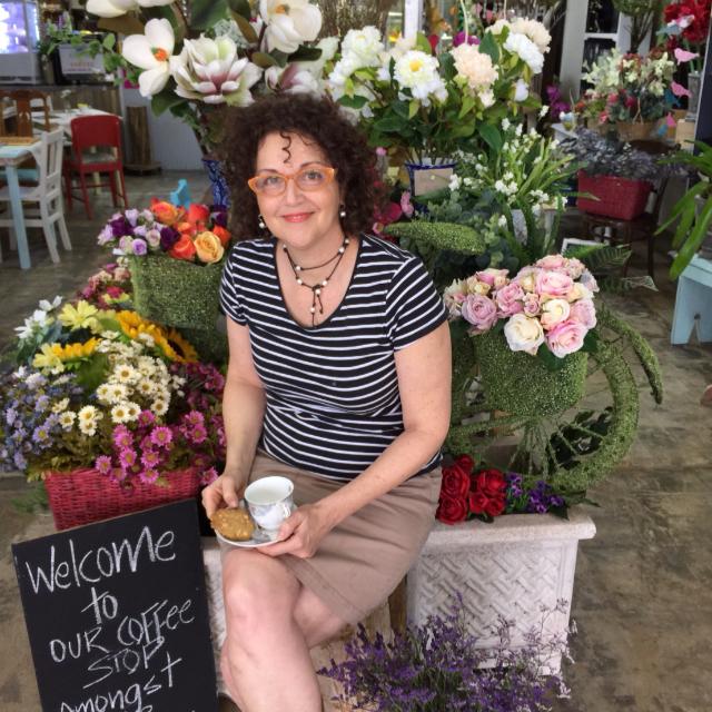A Lady Sitting next to the Cafe Sign with a Coffee — Your Local Florist in Ingham