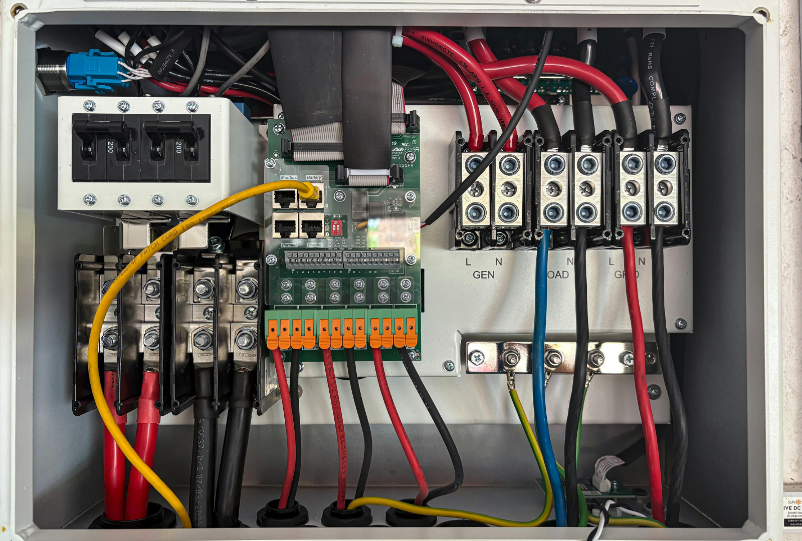 An open gray electrical junction box featuring wiring, terminal blocks, a circuit breaker, and a central circuit board.