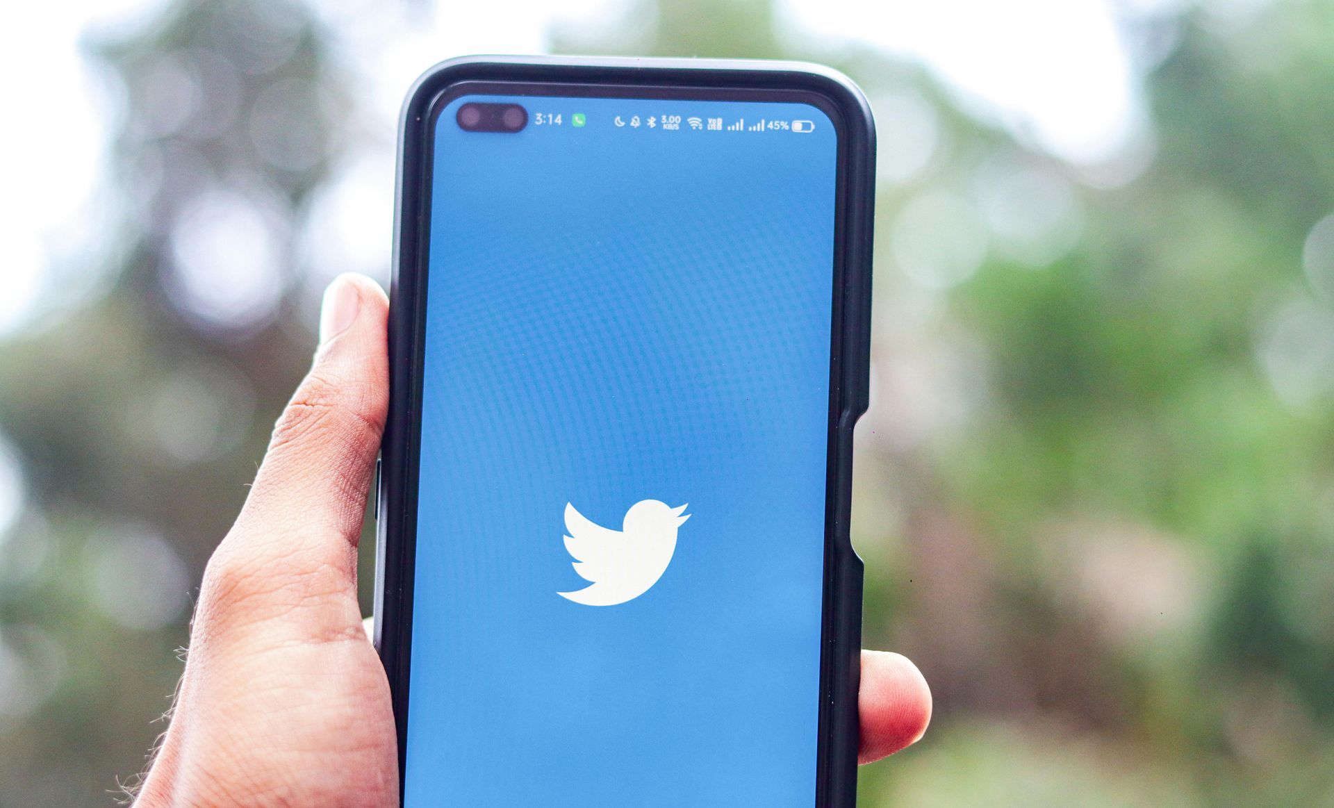 A person is holding a cell phone with a twitter logo on the screen