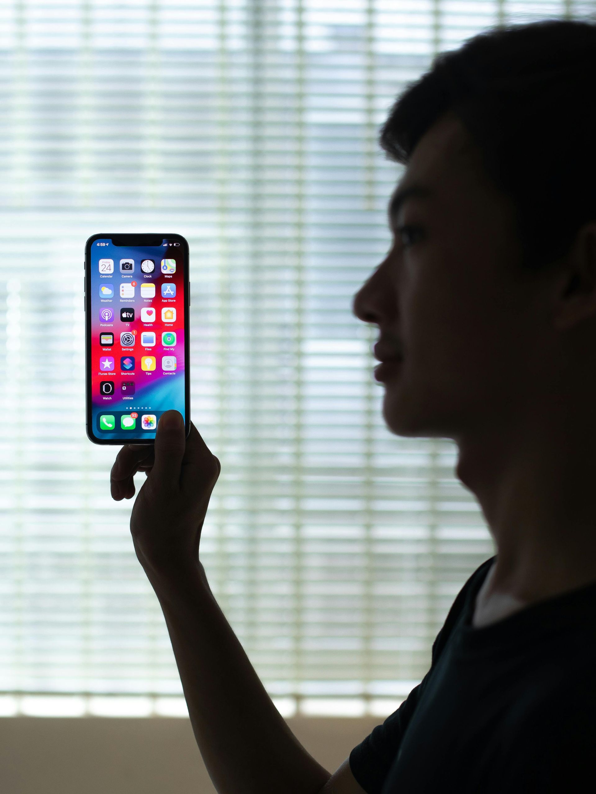 A man is holding a cell phone in front of a window