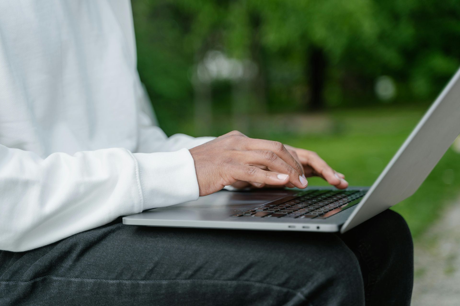 A person is typing on a laptop outside in the park