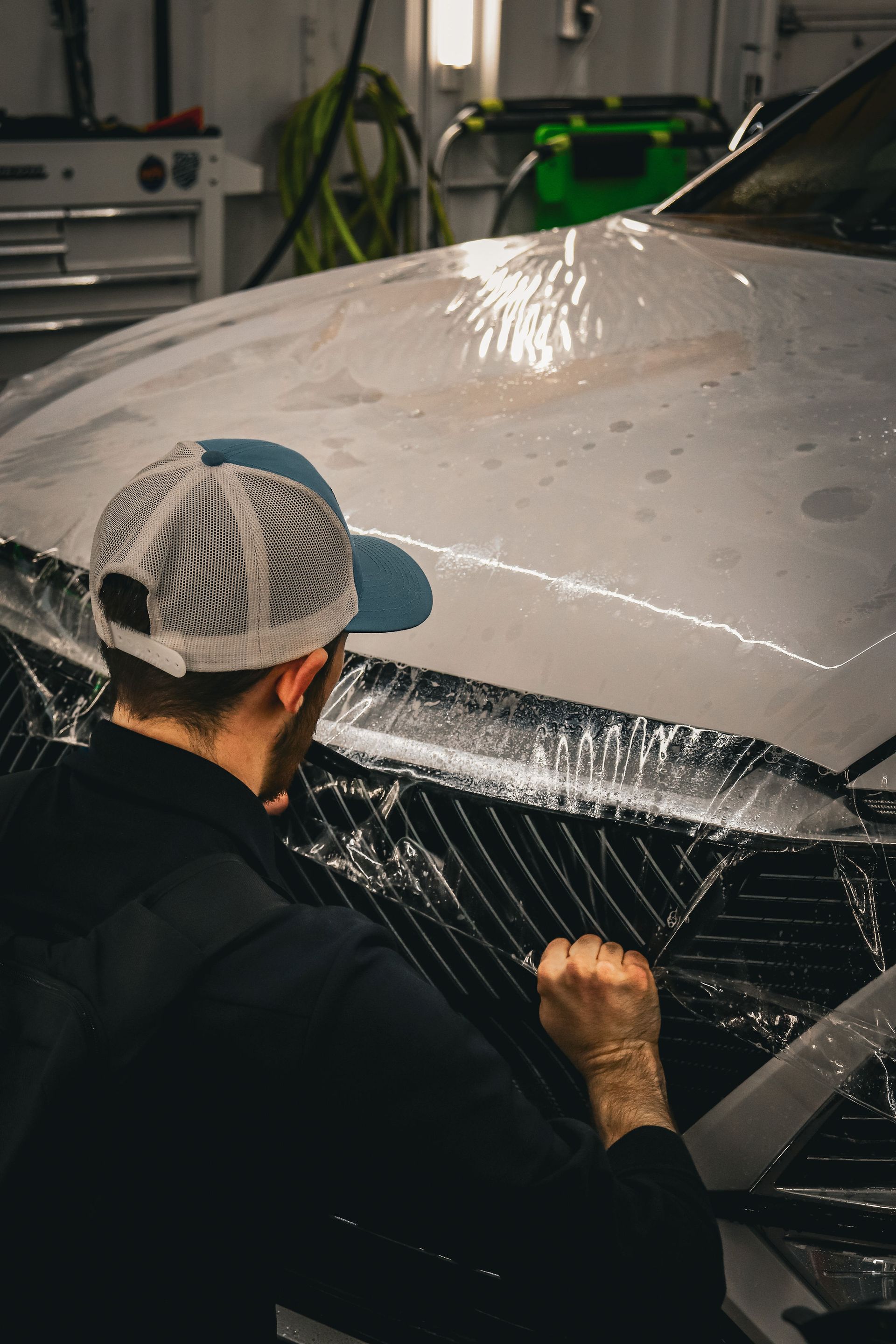 A man is wrapping the hood of a car with plastic wrap.