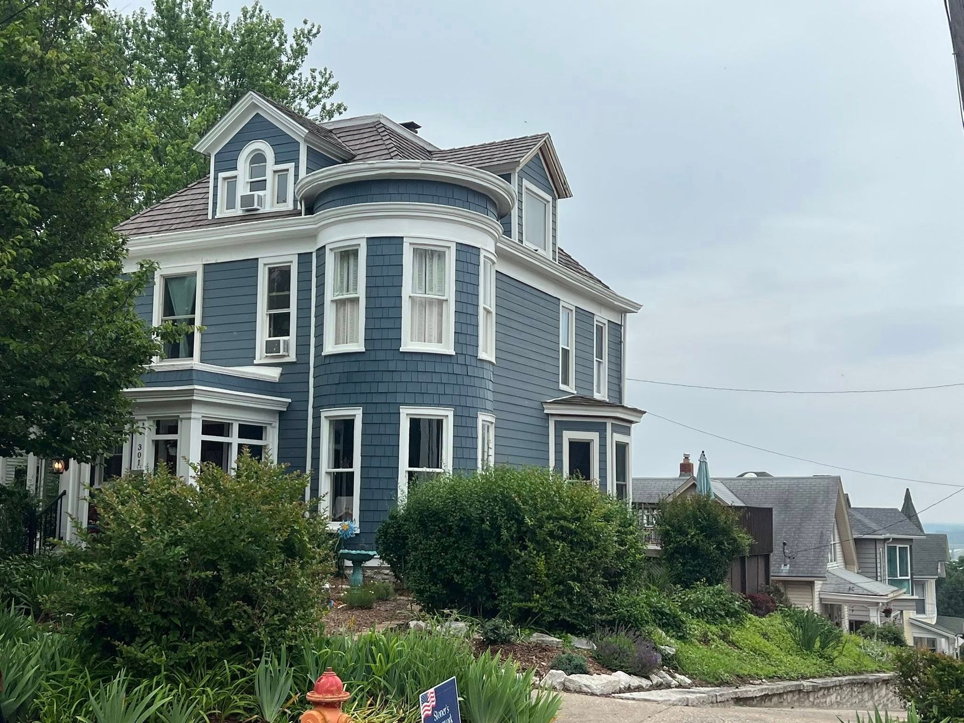Blue Victorian house with white trim, bay window, and partial view of surrounding houses.