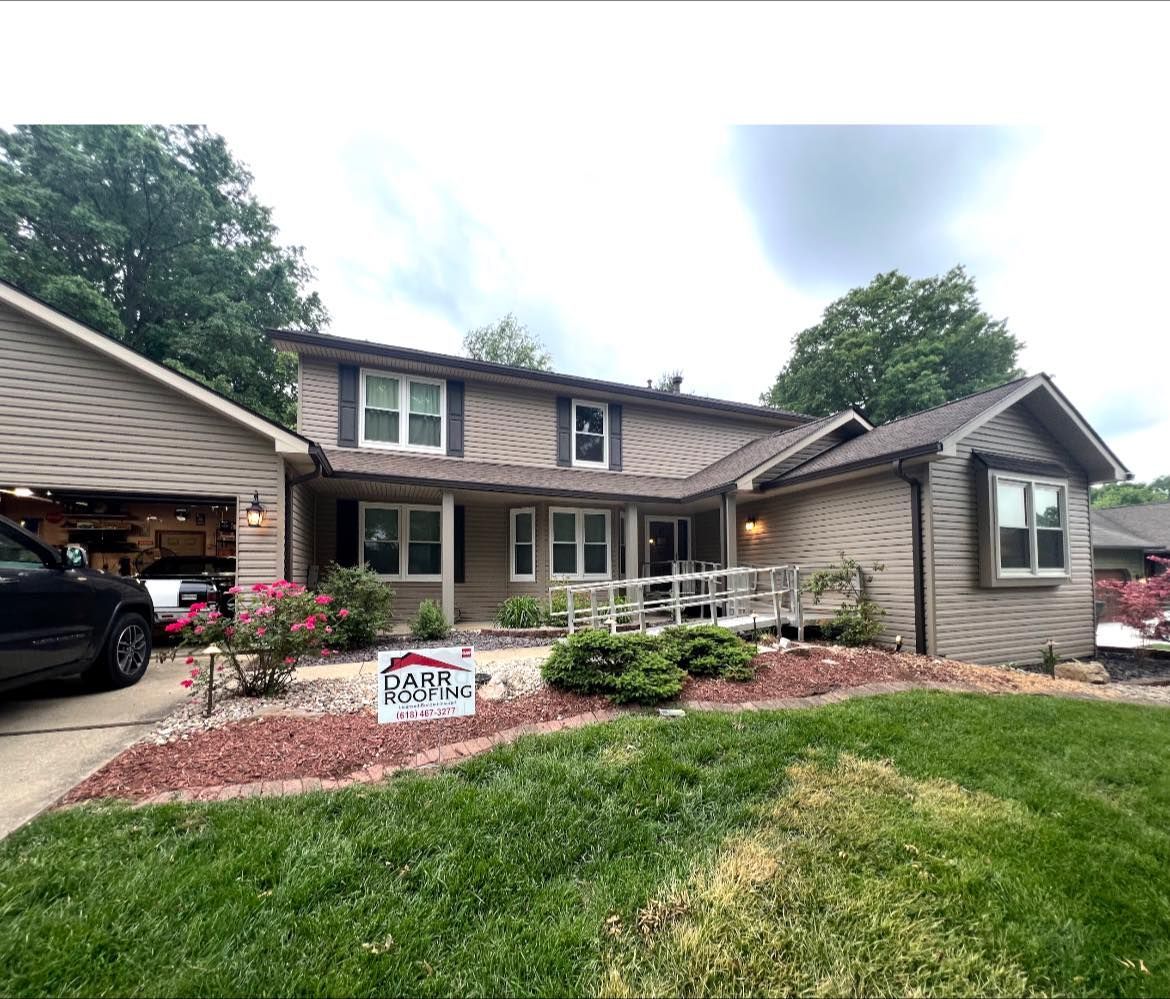 Two-story house with a wooden ramp, brown siding, and a detached garage, surrounded by landscaping.