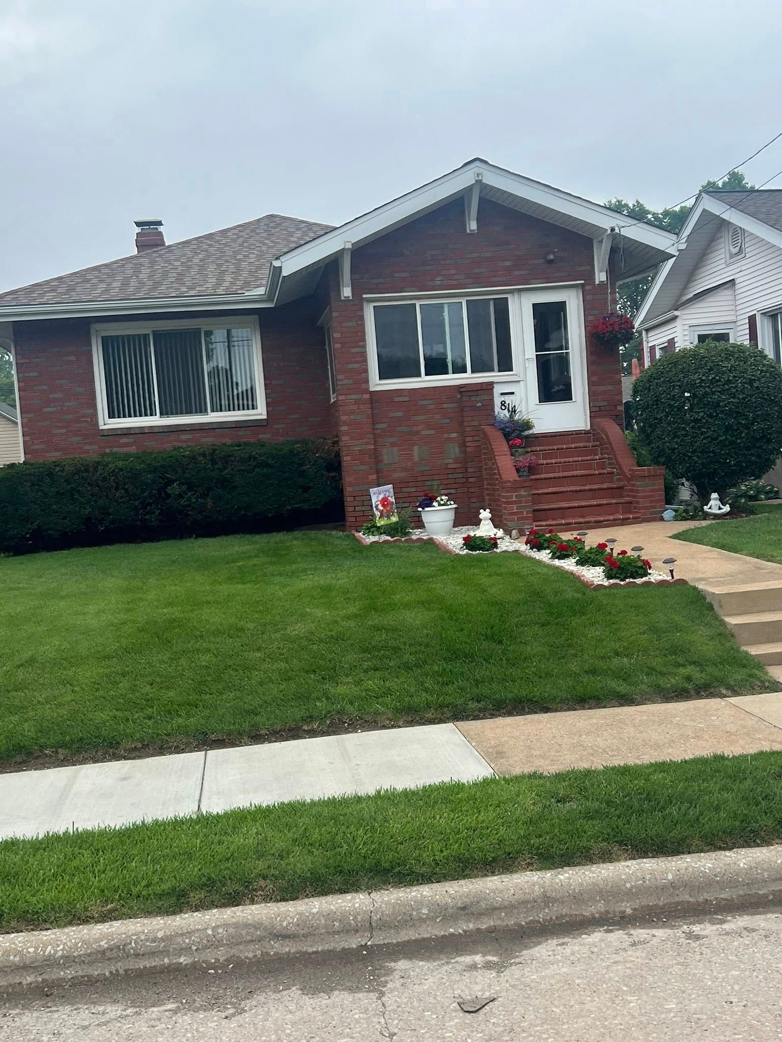 Red brick house with green lawn, steps up to white door, small flower decorations.