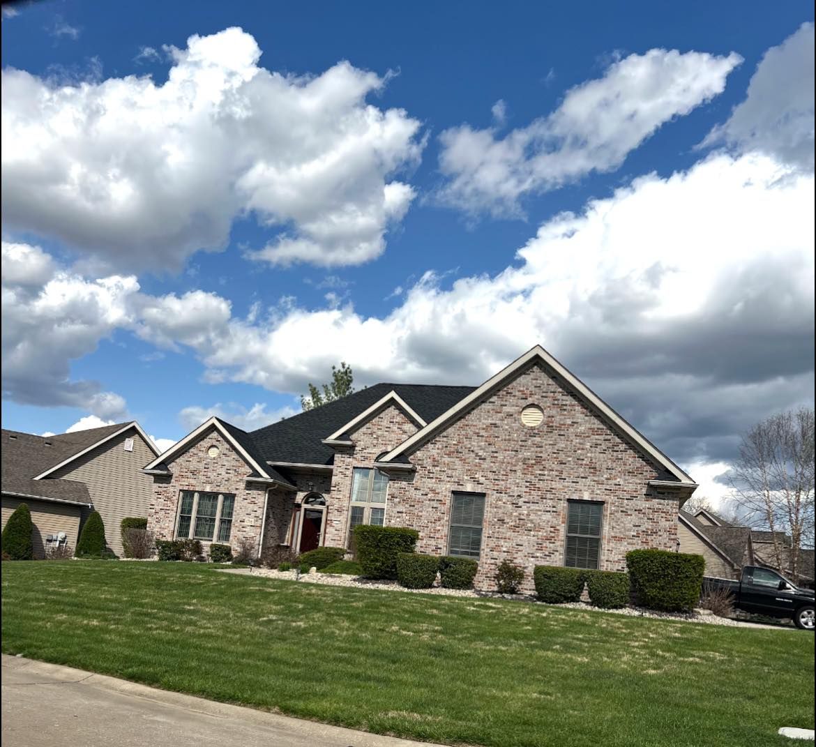 Brick house with green lawn, blue sky, and white clouds.