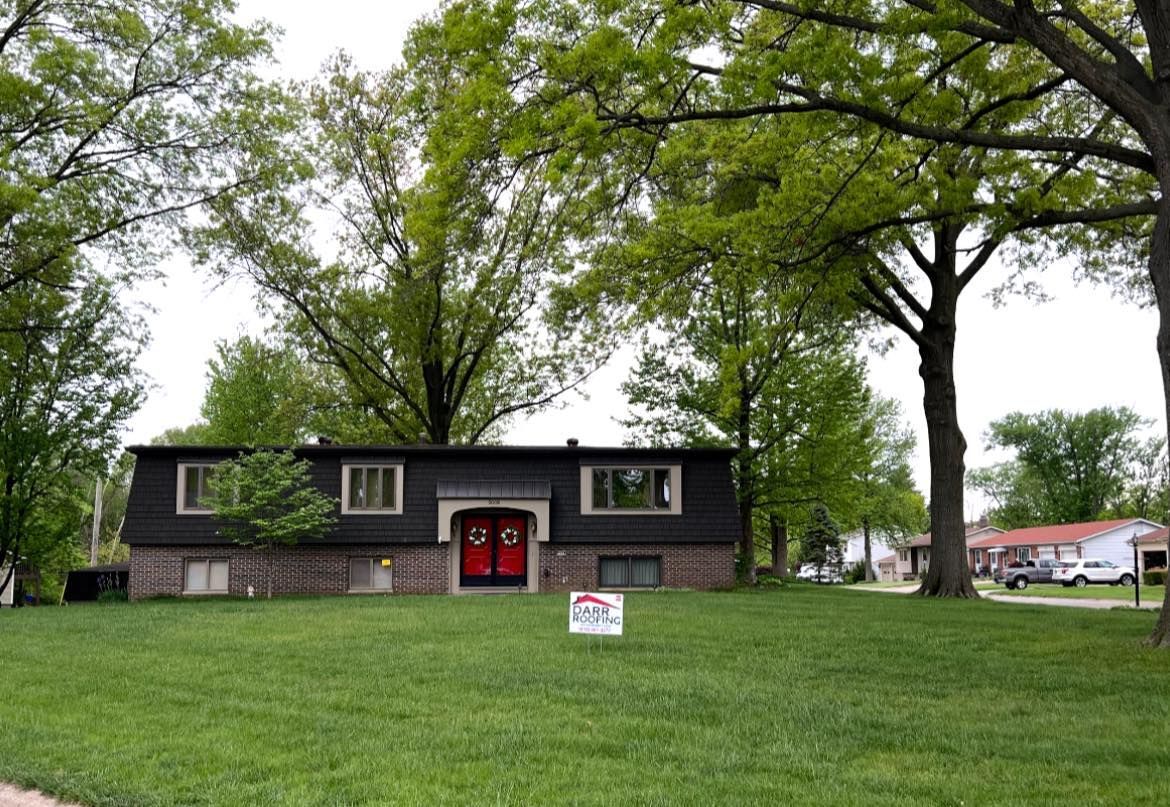 Two-story home with red doors and two windows. Green lawn, trees, and 