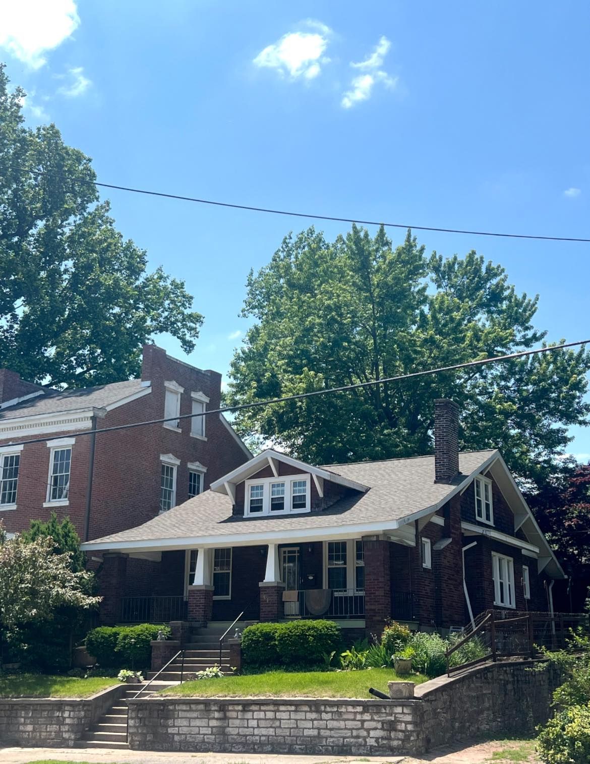 Brick houses with trees and blue sky. The closer house has a porch and dormer.