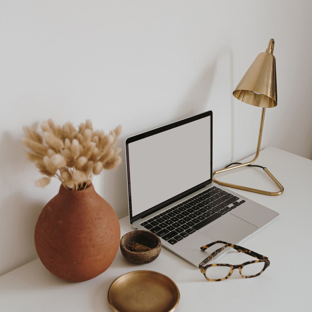 A Laptop is Sitting on a Desk Next to a Vase of Dried Flowers and a Lamp — TJL Business Advisors & Accountants in Taree, NSW