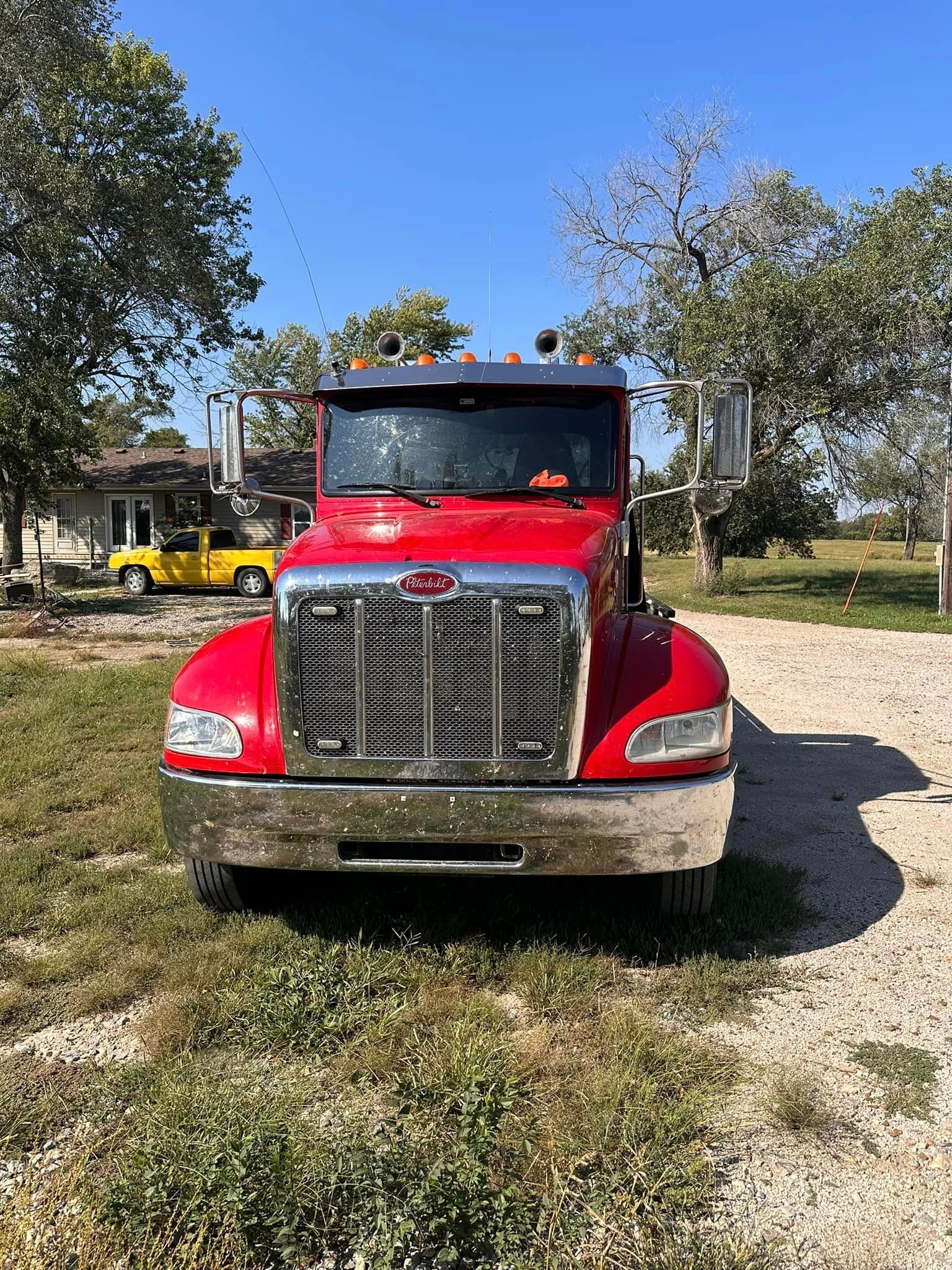 A red semi truck is parked in a gravel lot.