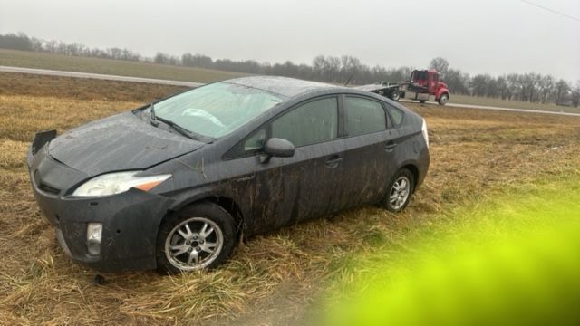 A gray prius is sitting in the middle of a field.
