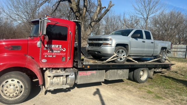 A tow truck is carrying a silver truck on the back of it.