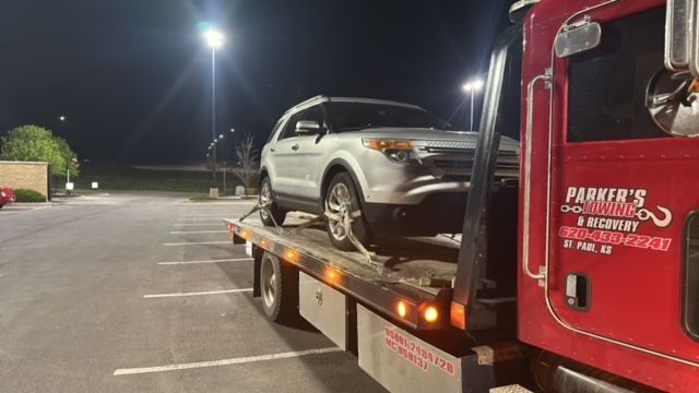 A tow truck is towing a car in a parking lot at night.