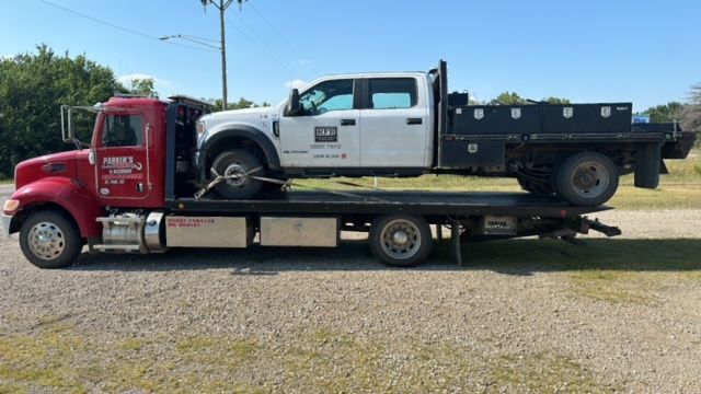A tow truck is carrying a white truck on the back of it.