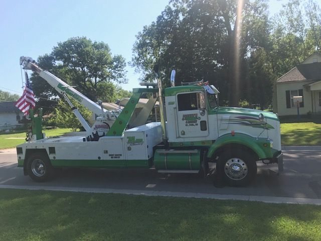 A green and white tow truck is parked in front of a house.