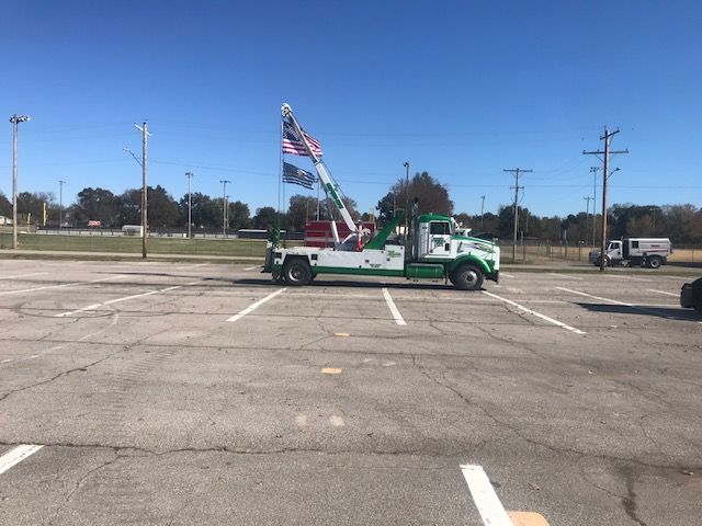A green and white tow truck is parked in a parking lot.