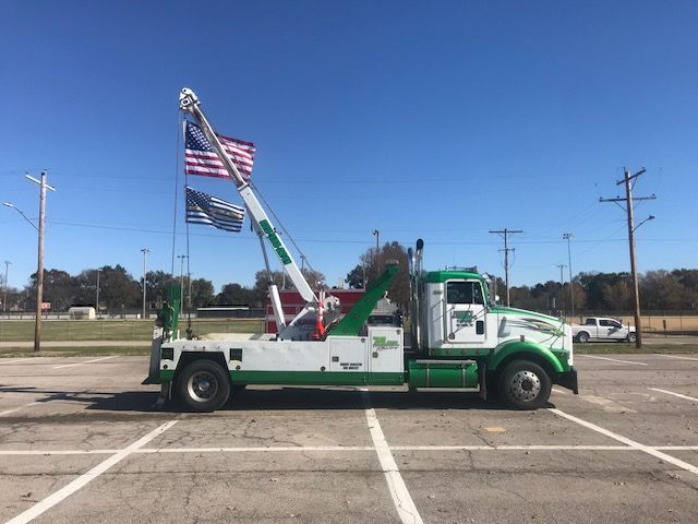 A green and white tow truck is parked in a parking lot.