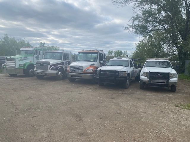 A row of tow trucks are parked in a gravel lot.