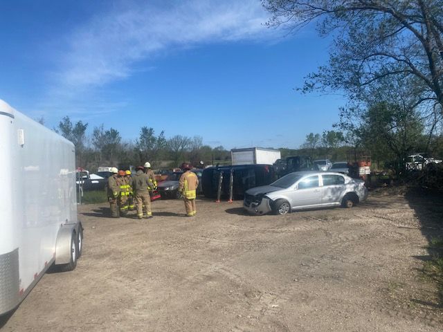 A group of firefighters are standing in a parking lot next to a car.