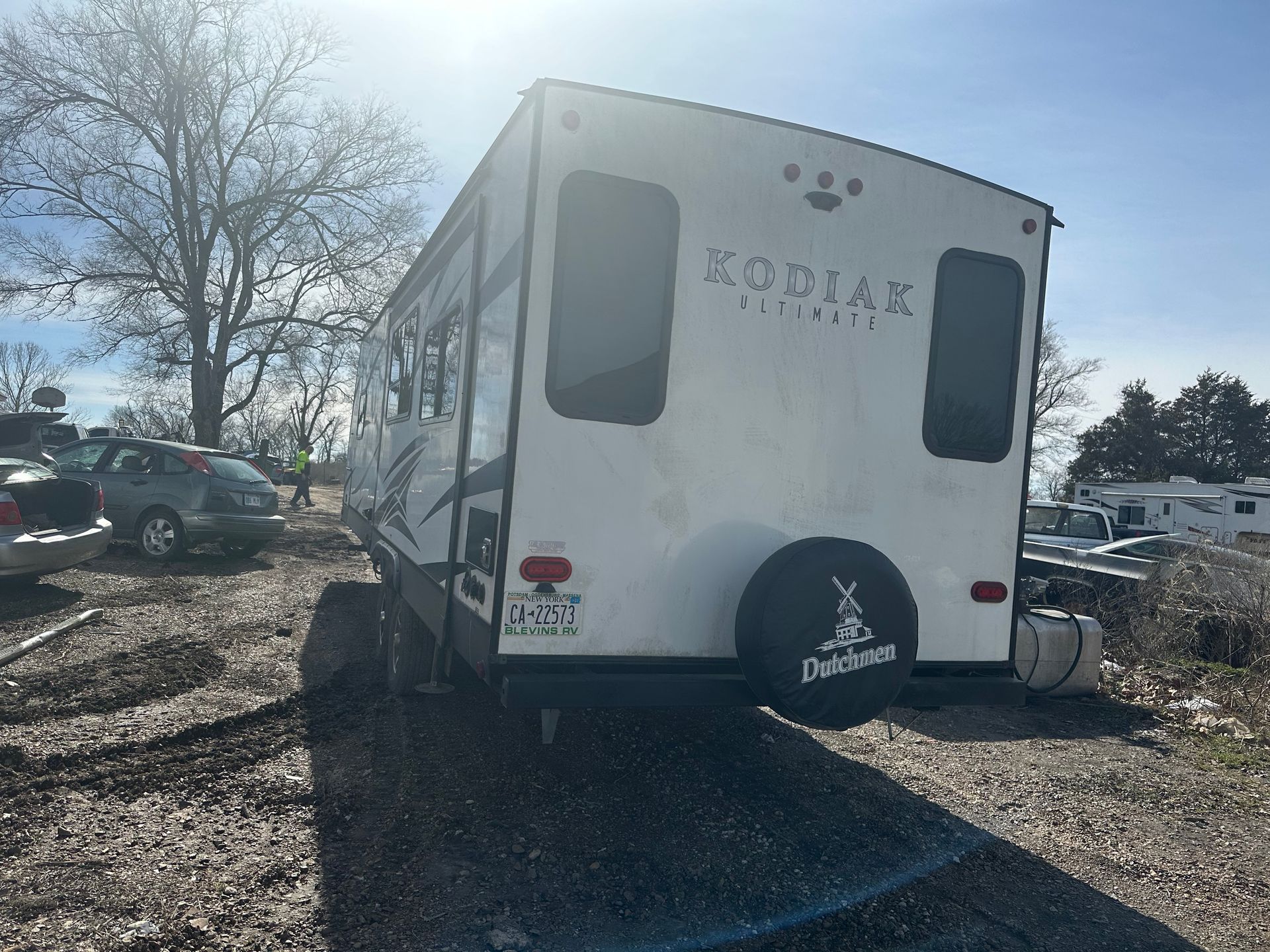A white zodiac trailer is parked in a gravel lot