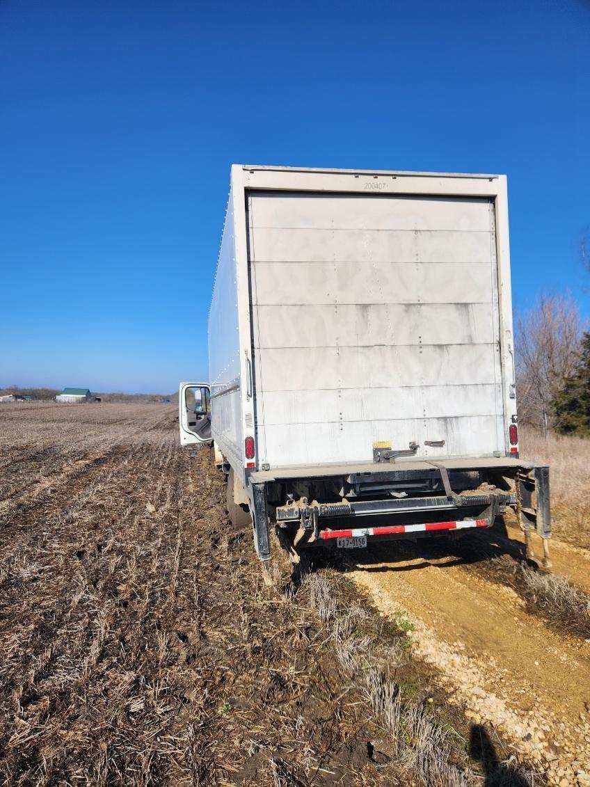 A white semi truck is driving down a dirt road in a field.