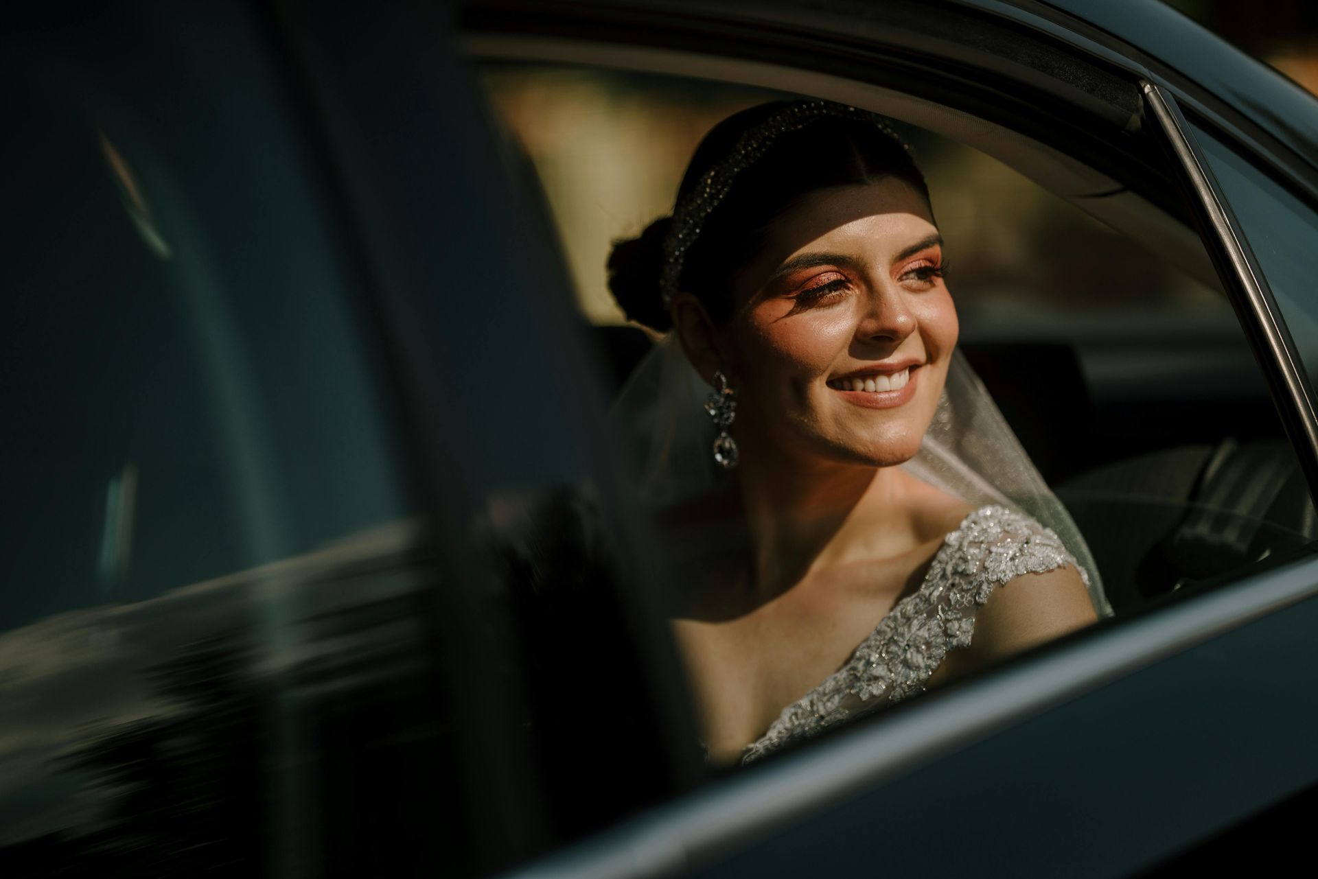 A bride in a wedding dress is sitting in a car and smiling.