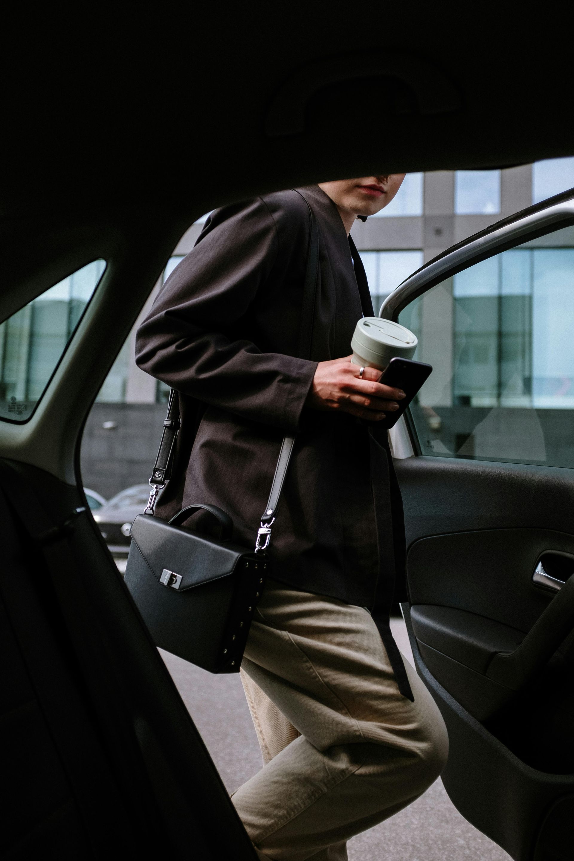 A woman is getting out of a car holding a cup of coffee and a cell phone.