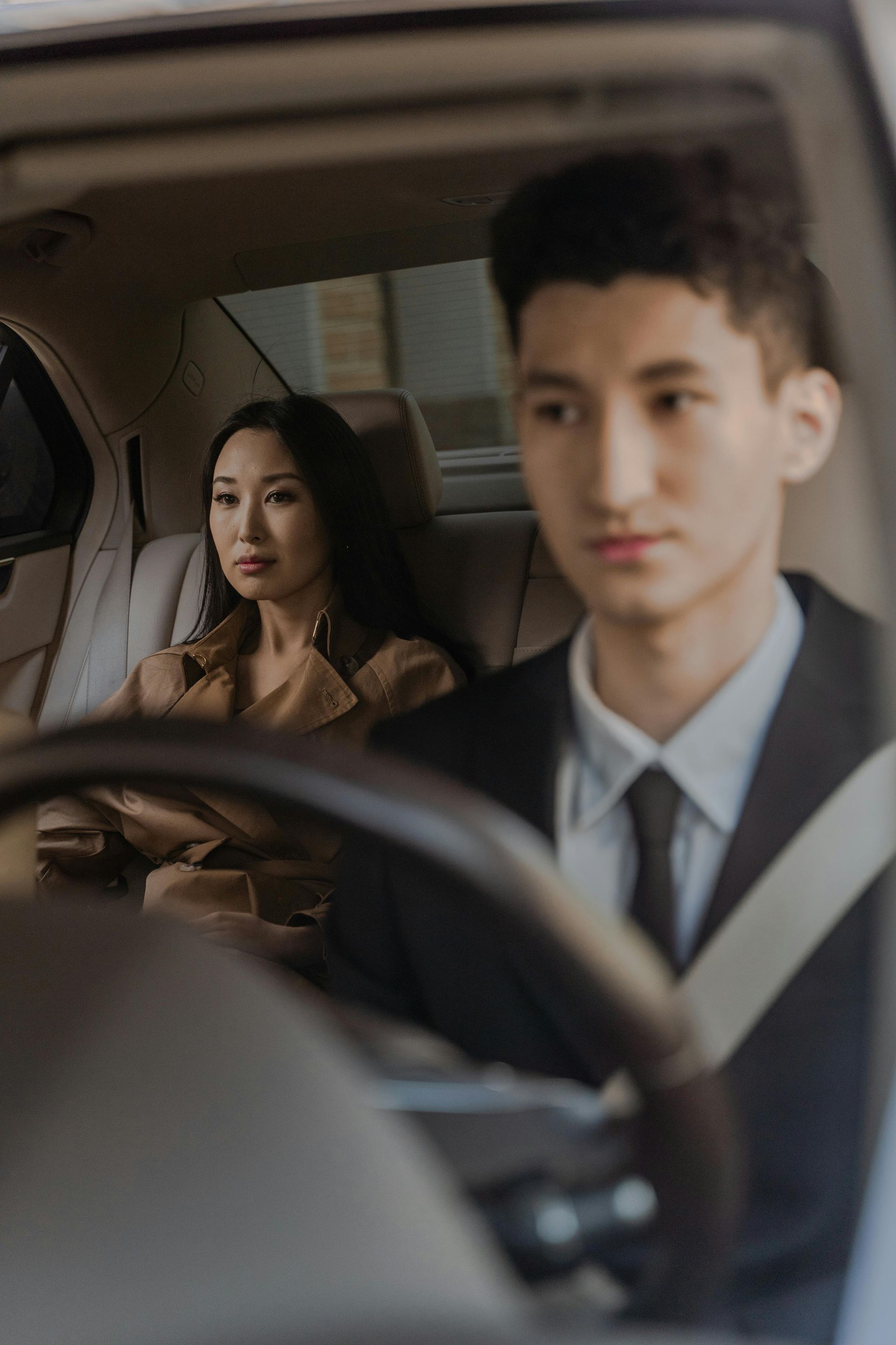 A man in a suit and tie is driving a car with a woman in the back seat.
